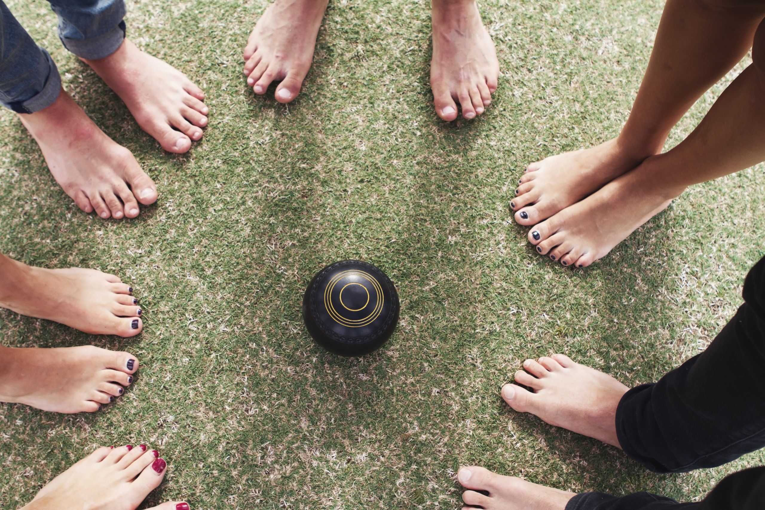 Overhead view of bare feet friends on grass around lawn bowls